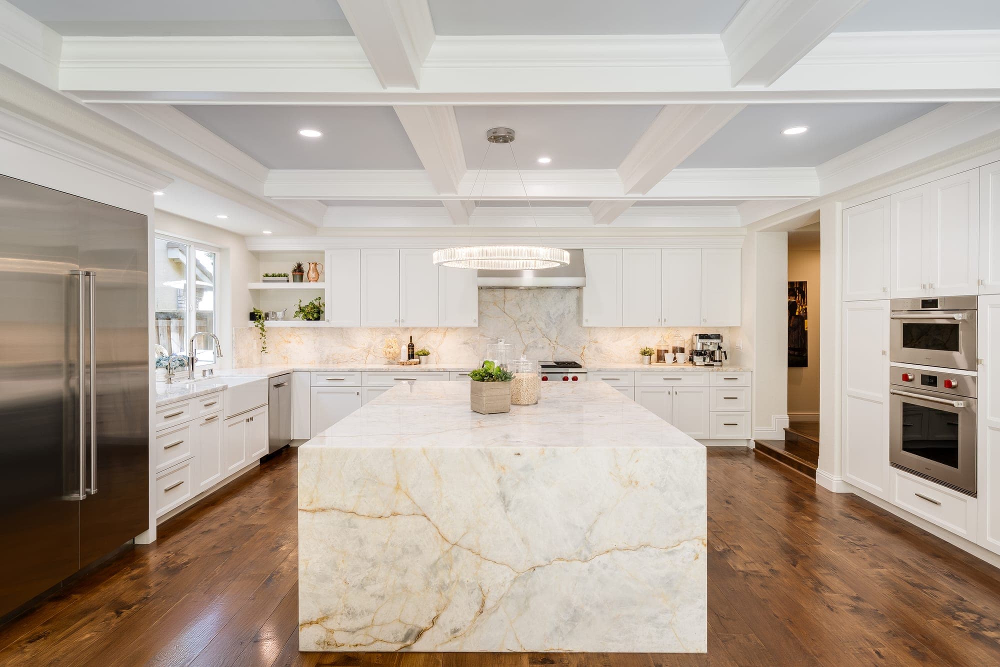 The renovated kitchen with a quartzite waterfall island, white cabinetry, and stainless appliances.