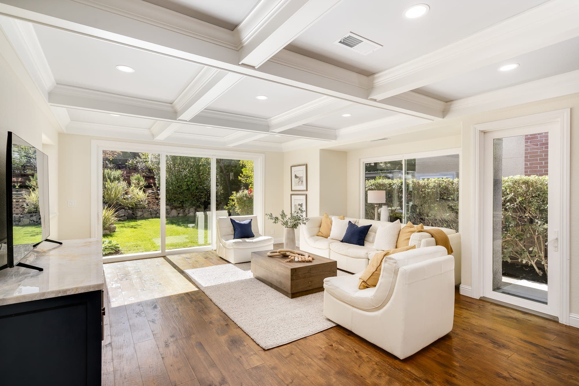 The family room with a coffered ceiling and wide glass doors opening to the backyard lawn.