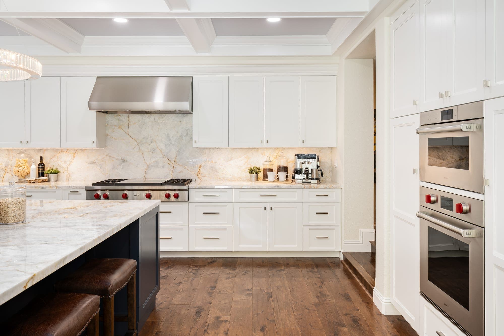A Wolf range under a stainless hood, set against a quartzite backsplash, with wall ovens beside it.