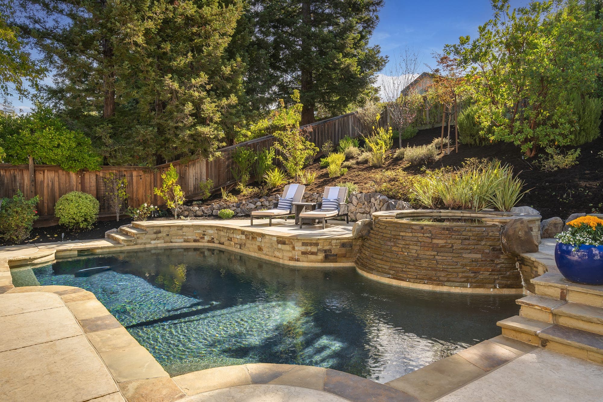 The pool with an elevated stone spa and cascading waterfall, framed by mature trees.