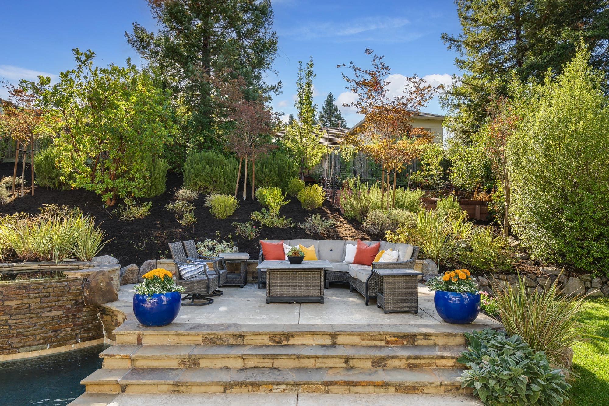A raised stone patio with lounge seating among planted beds.