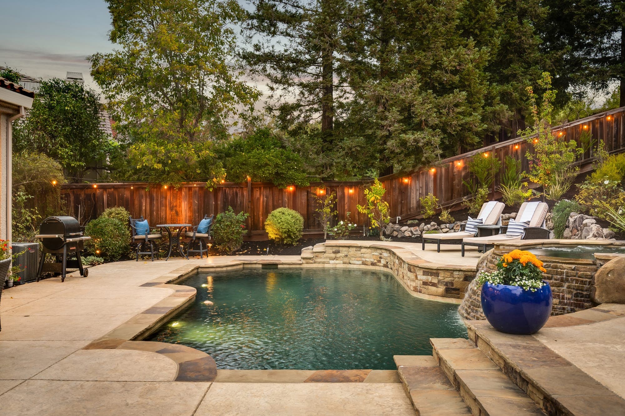 The pool and spa at dusk, with string lights along the fence.