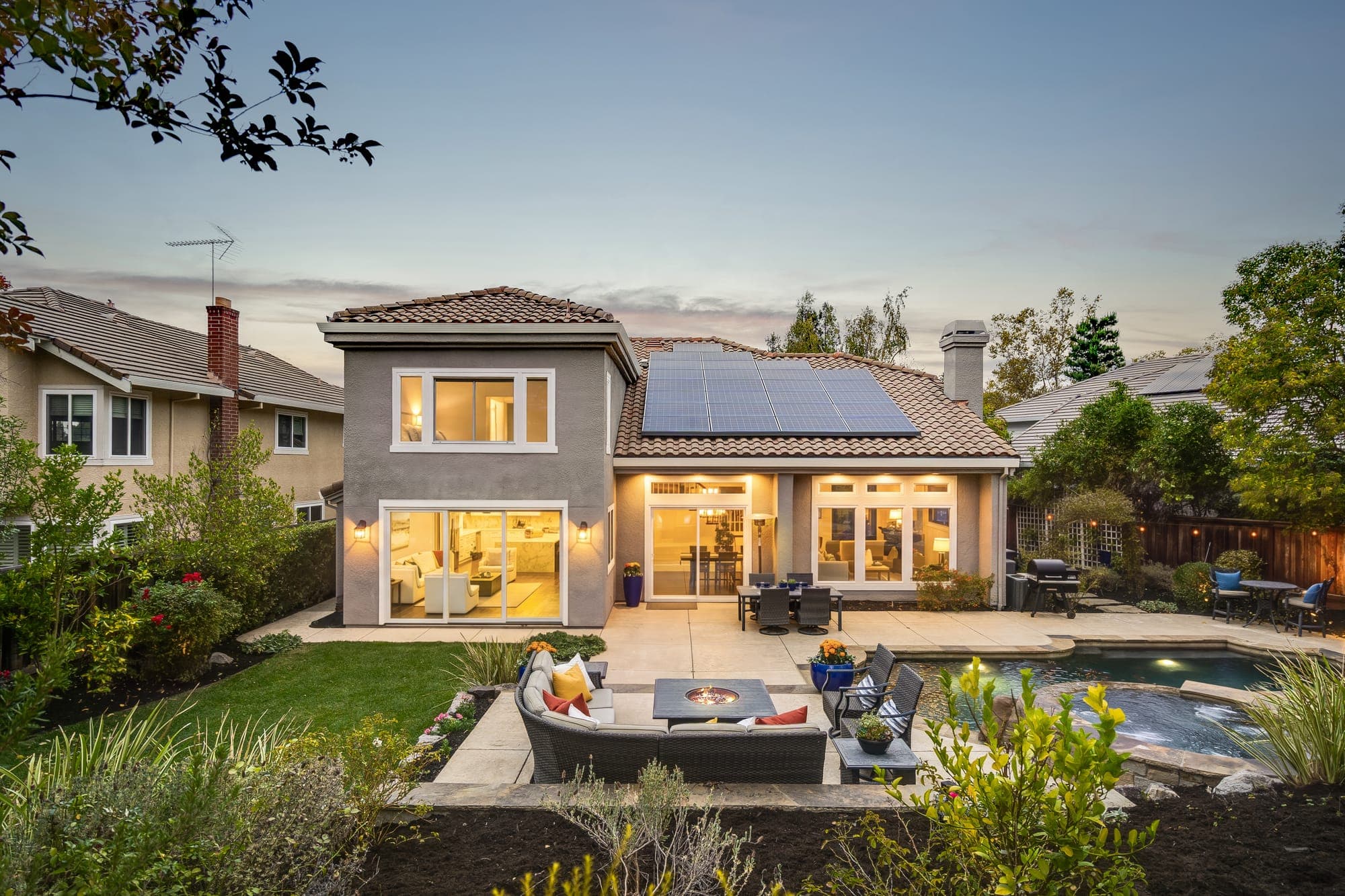 The back of the home at dusk, lit from within, across the lawn and lounge.