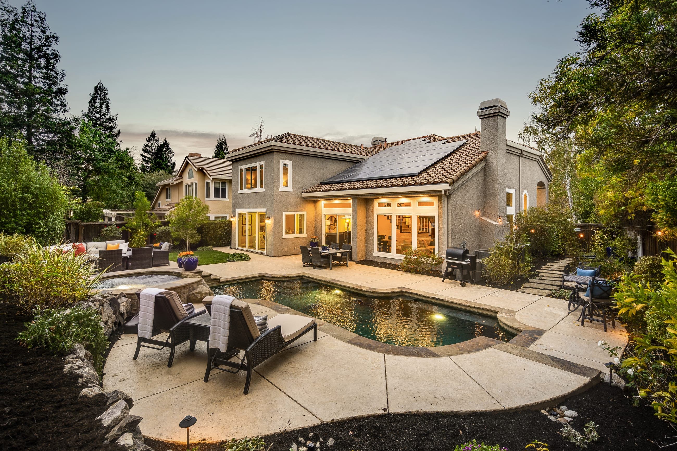 The backyard at dusk, with the pool and the lit home beyond.